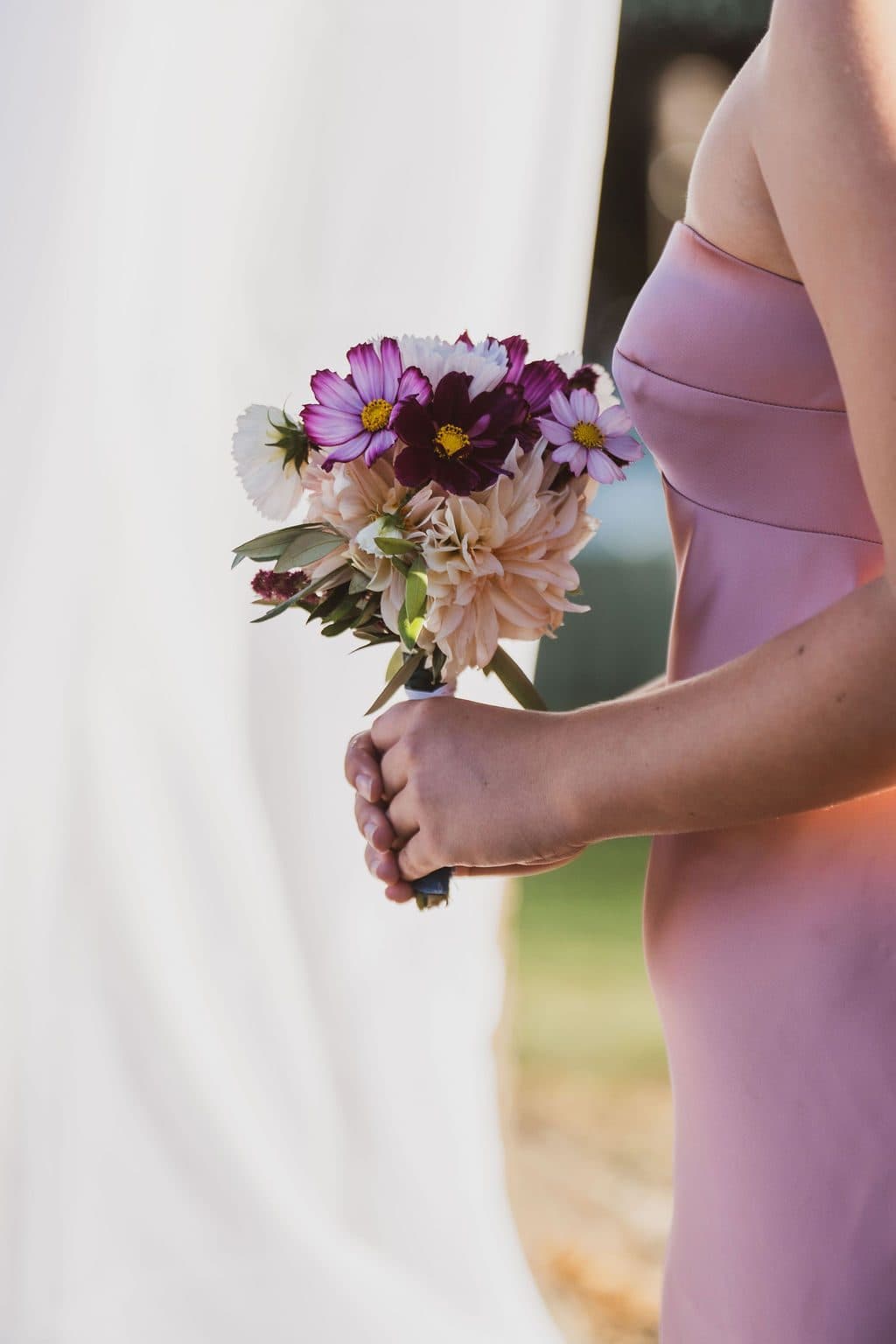 A bridesmaid holds a hand-tied bouquet of dahlias and cosmos grown on the family property