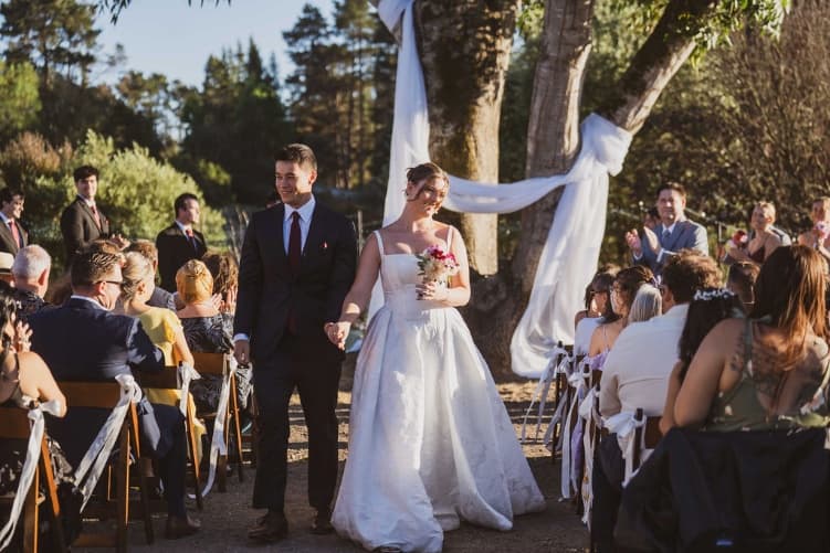 Damien and Claire walk back up the aisle as newlyweds under the trees