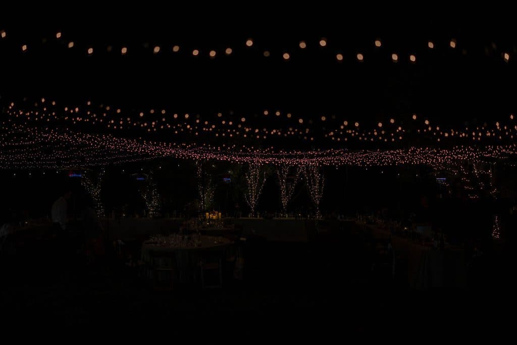A canopy of string lights glowing over the reception tables at night